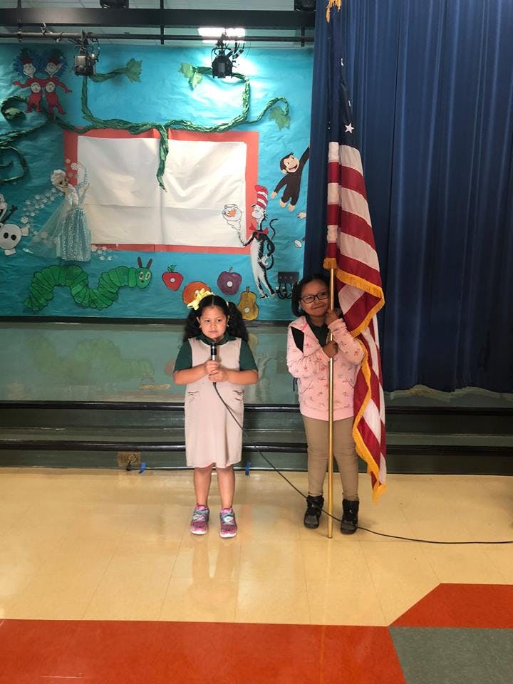 Two children standing, one holding a microphone and the other holding a flag