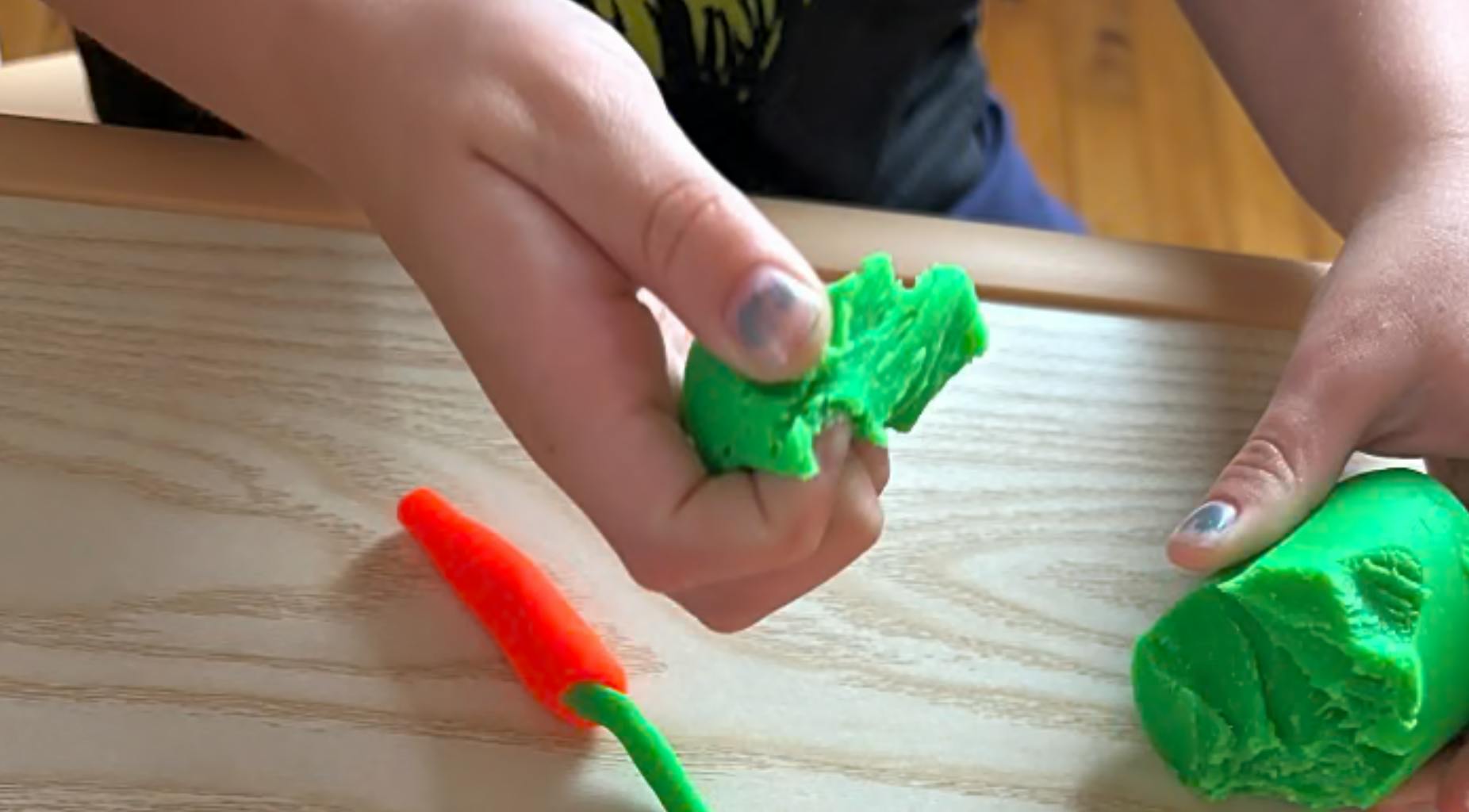 Person's hands molding green playdough