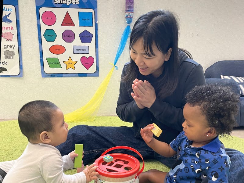 Adult and two children playing with shape sorter toys in a classroom