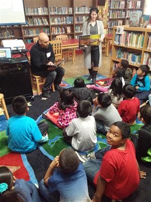 Two adults reading to a group of children in a library