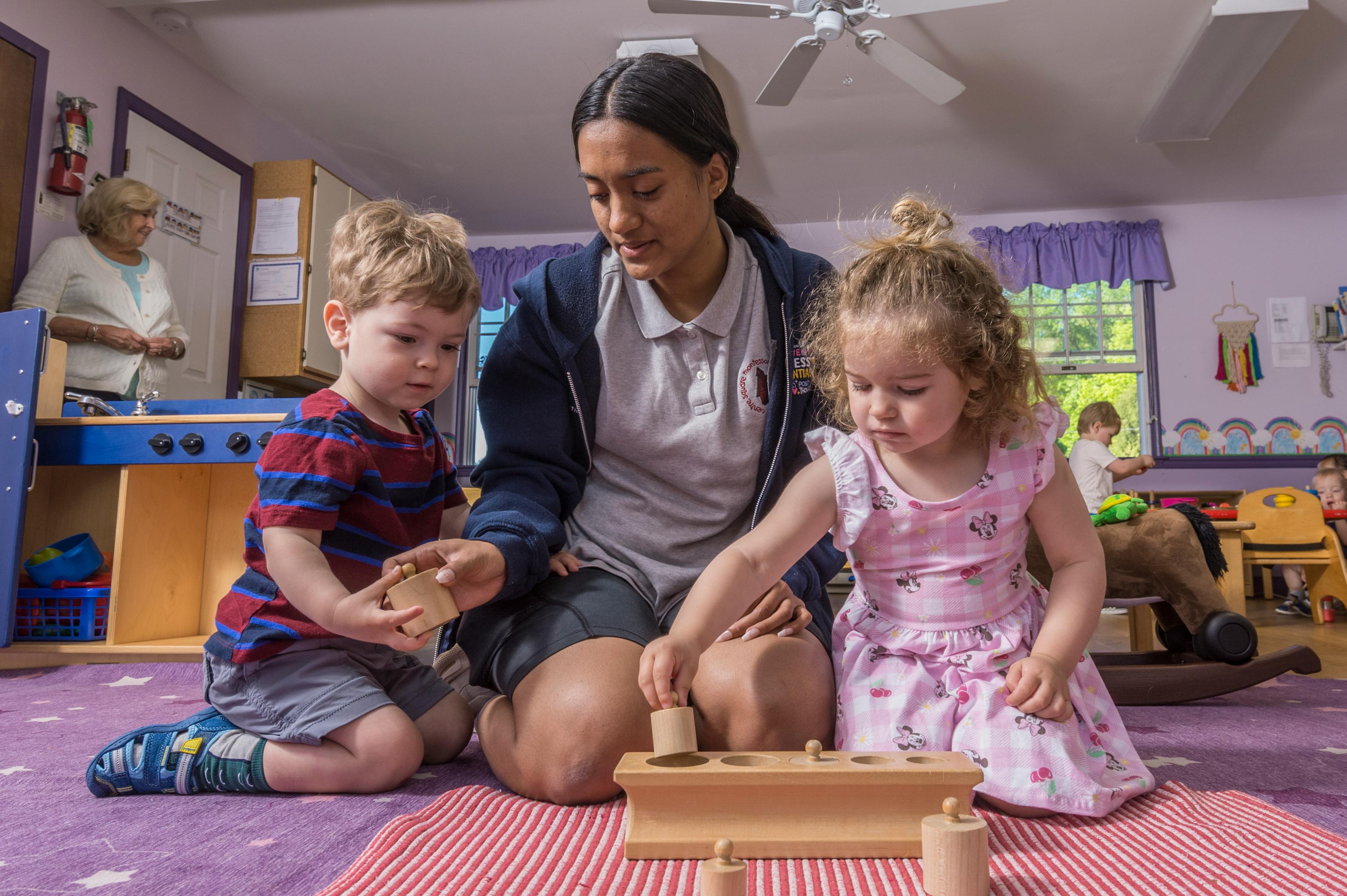 Person and two children playing with wooden blocks on the floor
