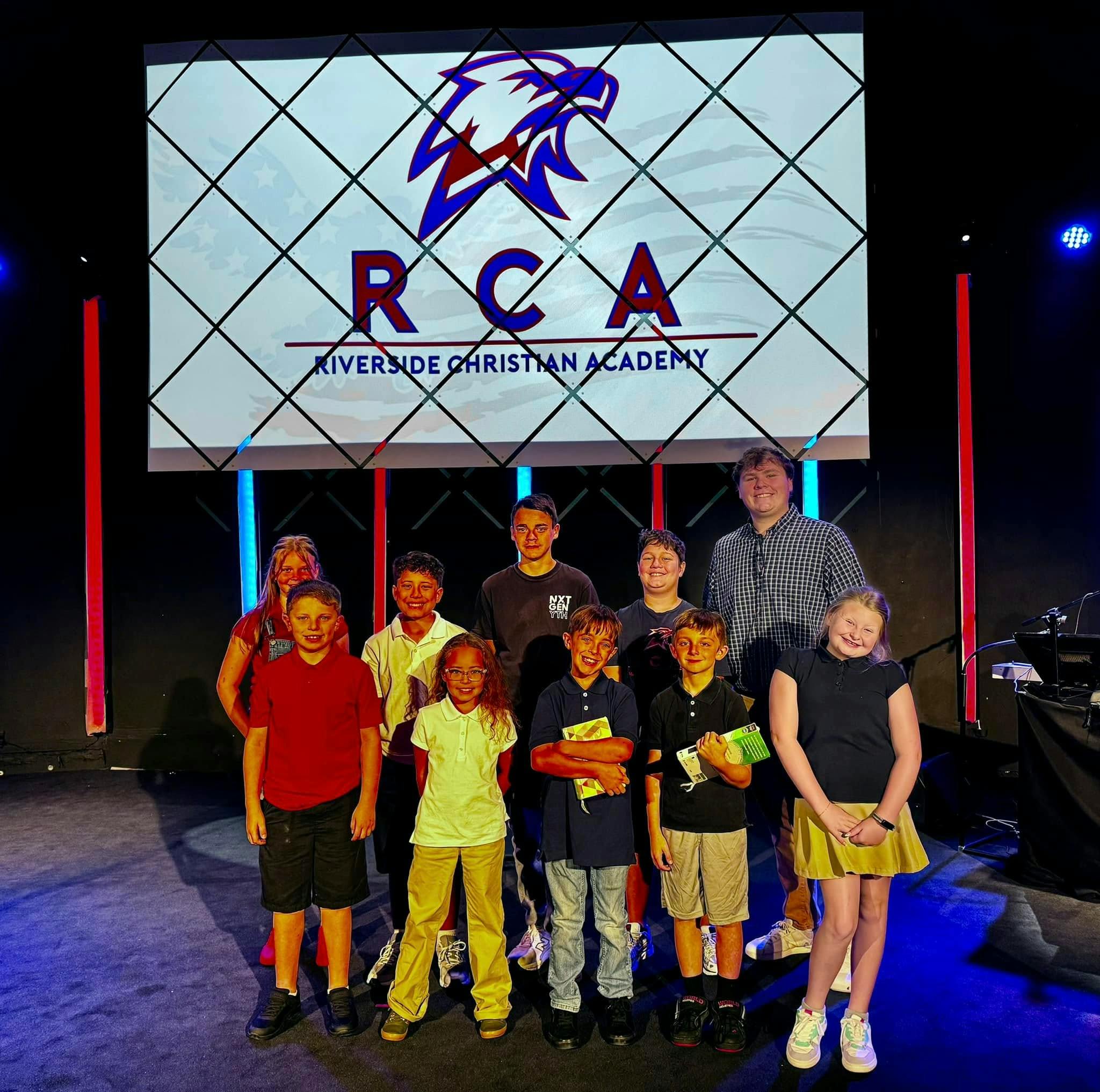 Group of adults and children standing in front of a screen with "RCA" logo