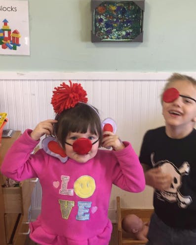 Child wearing a red clown nose and ears, another child wearing an eye patch