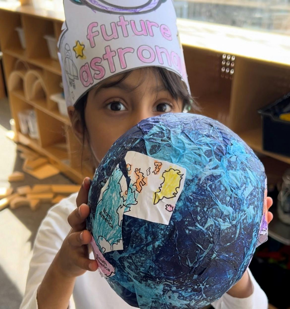 Child wearing a "Future Astronomer" crown holding a paper mache globe