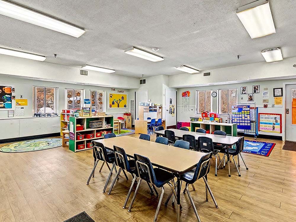 Classroom with tables and chairs, shelves of toys and books, and windows