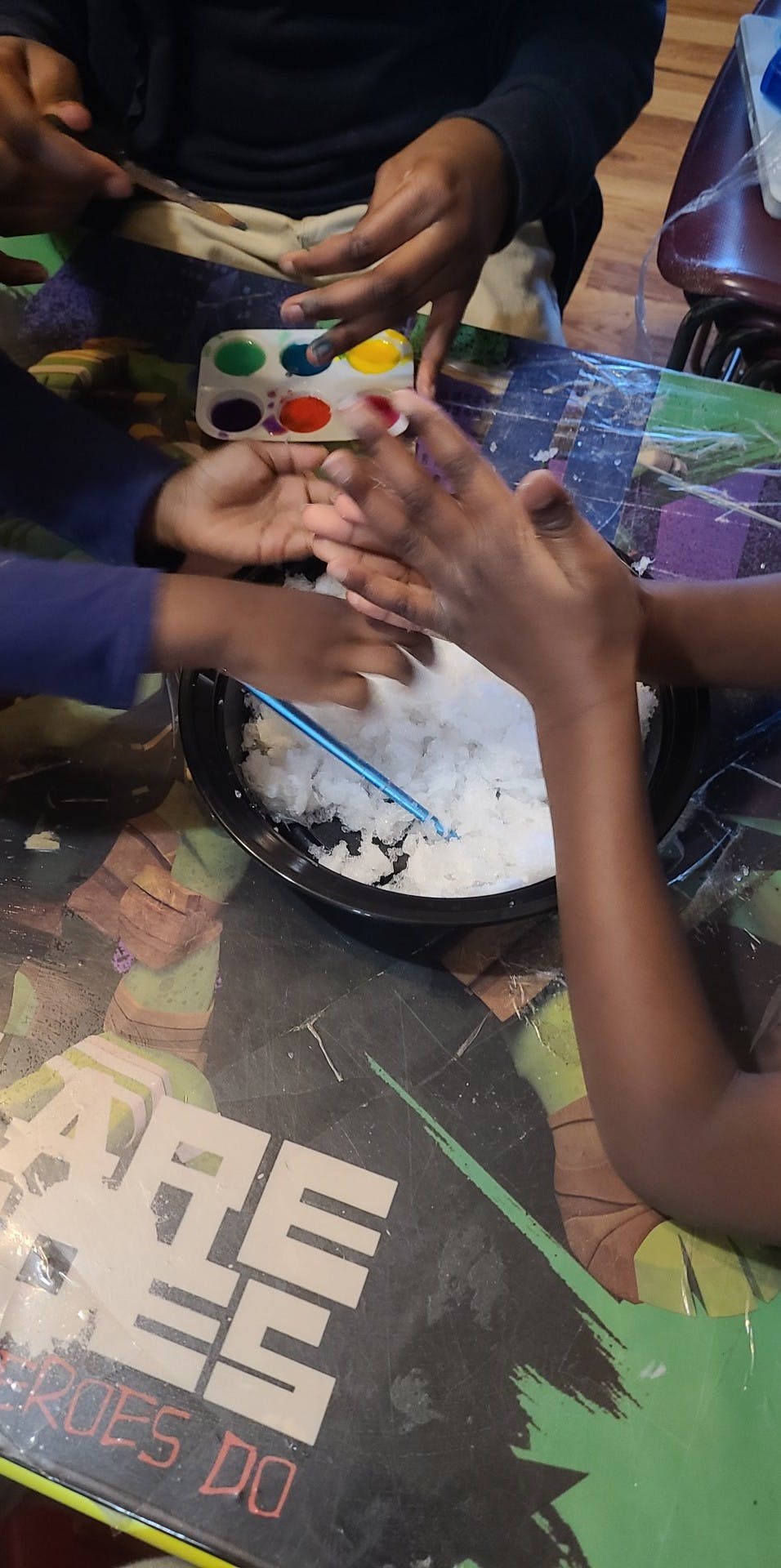 multiple children playing with a bowl of ice and a paint palette