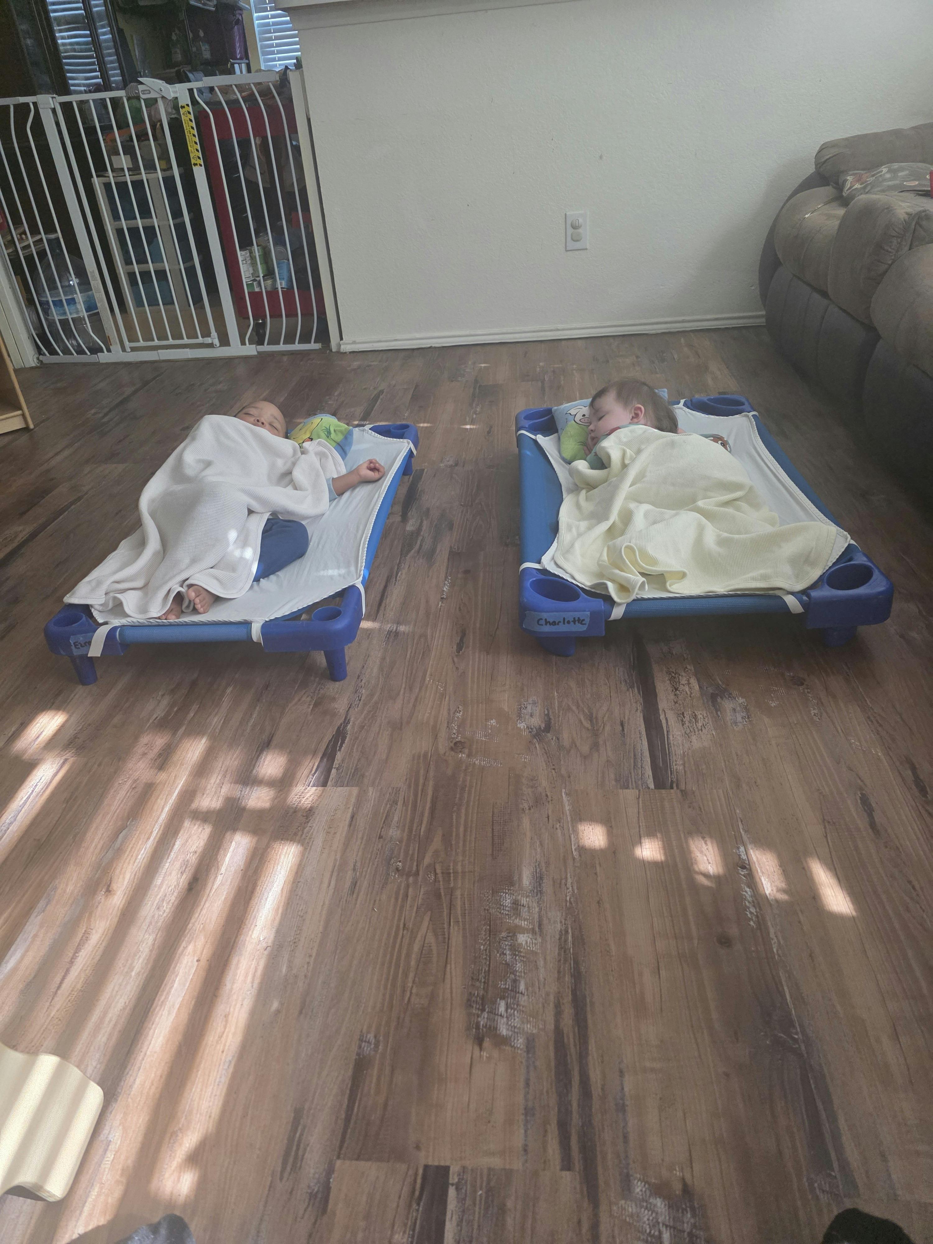 Two children sleeping on cots on a wooden floor