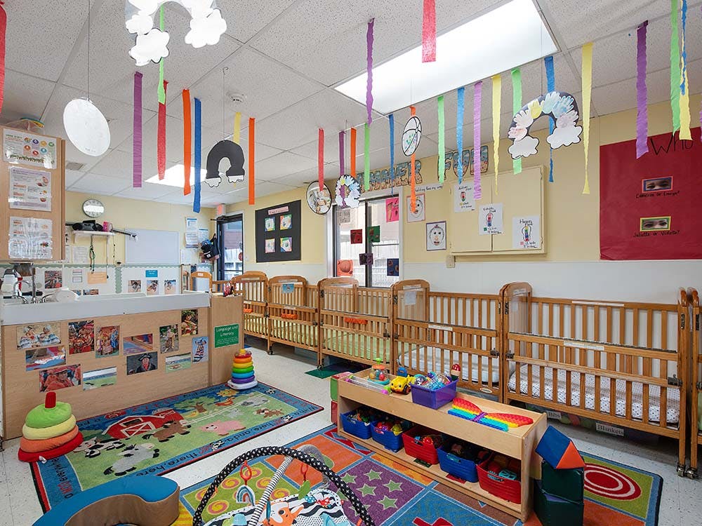 Classroom with cribs, colorful rugs, and decorations hanging decorations