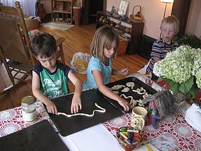 Two children making cookies on baking sheets, another child watching