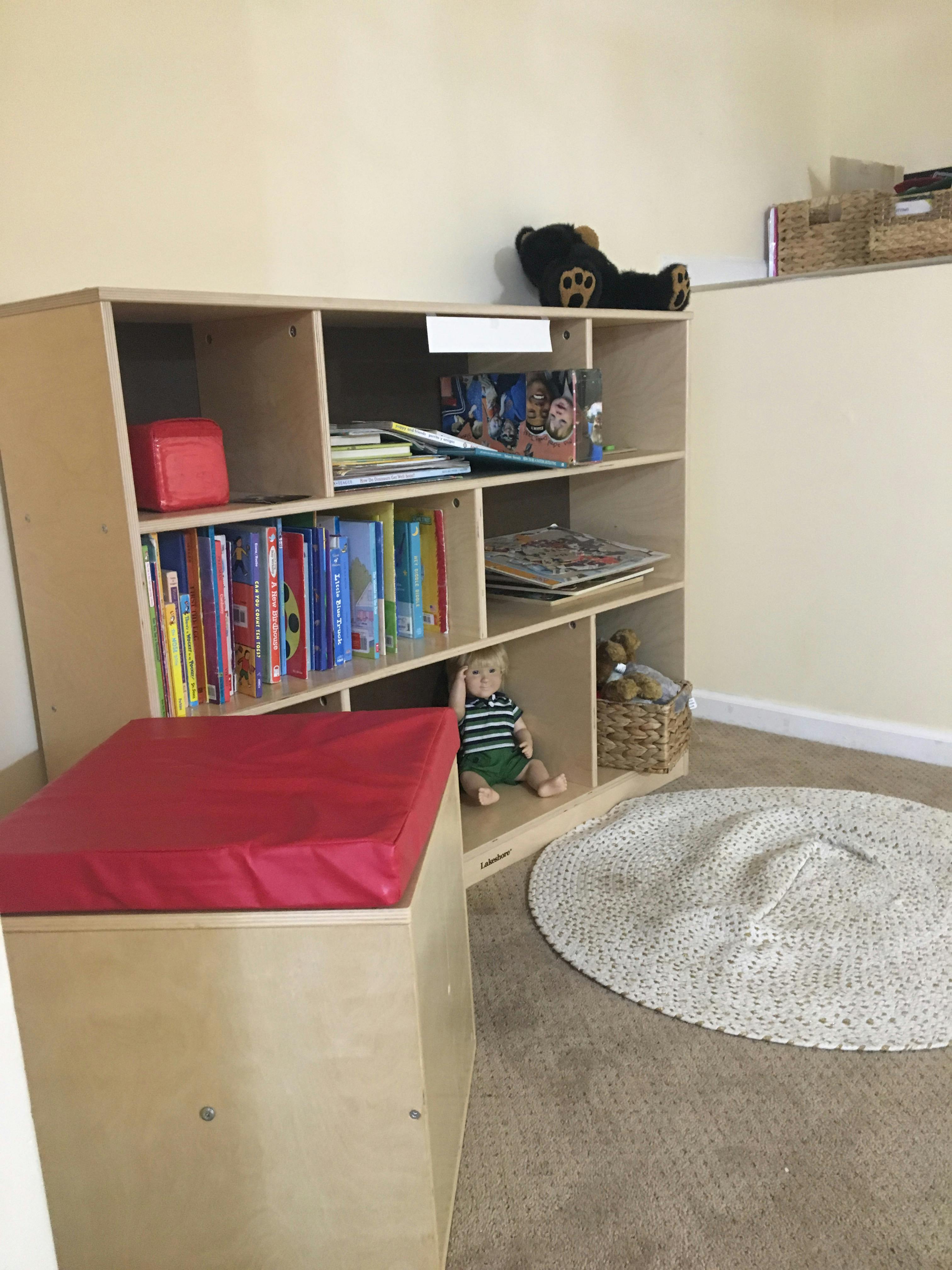 Bookshelf with books, a red cushion, and a doll in a classroom