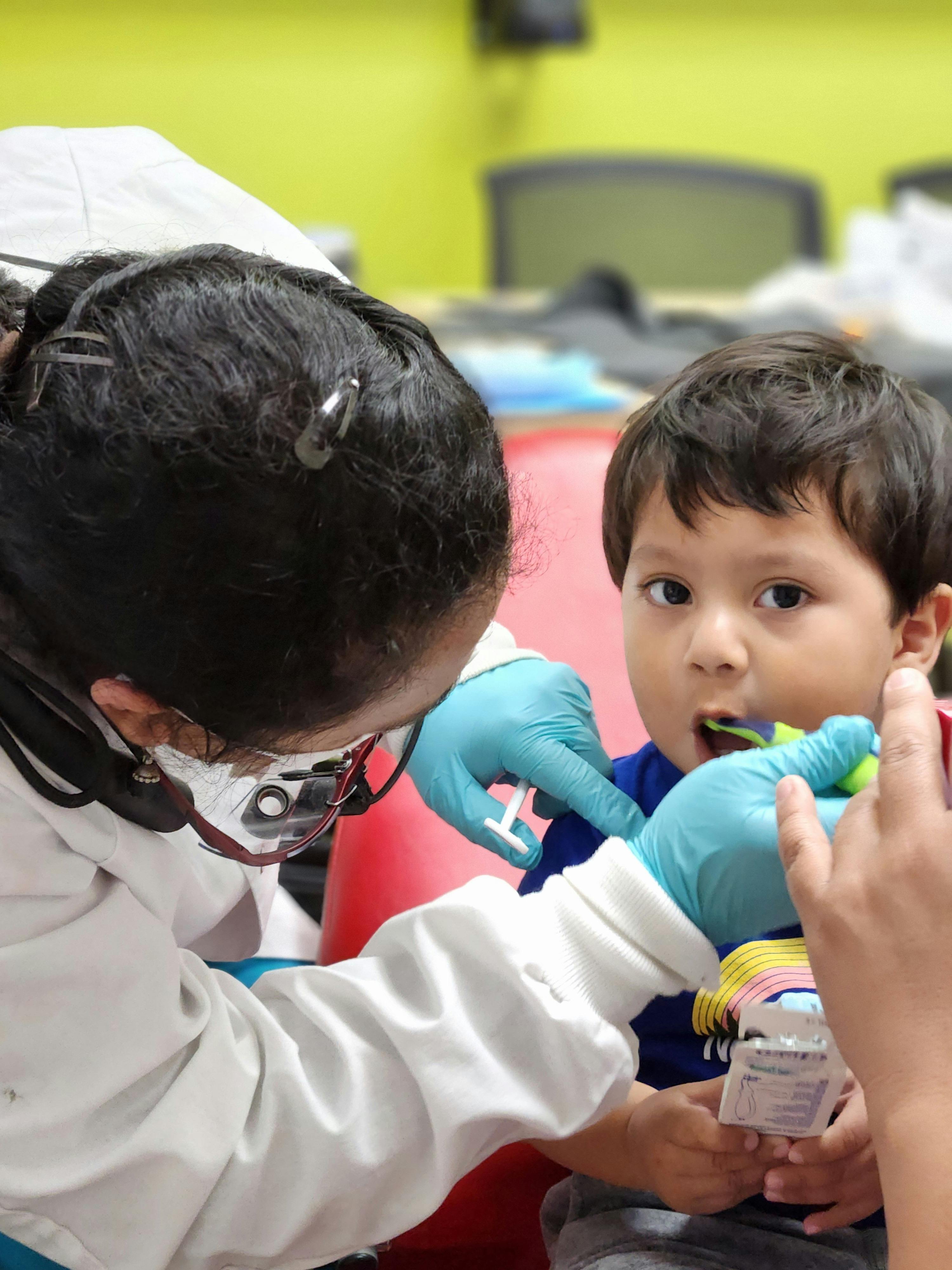 Person in medical attire with gloves examining a child's mouth