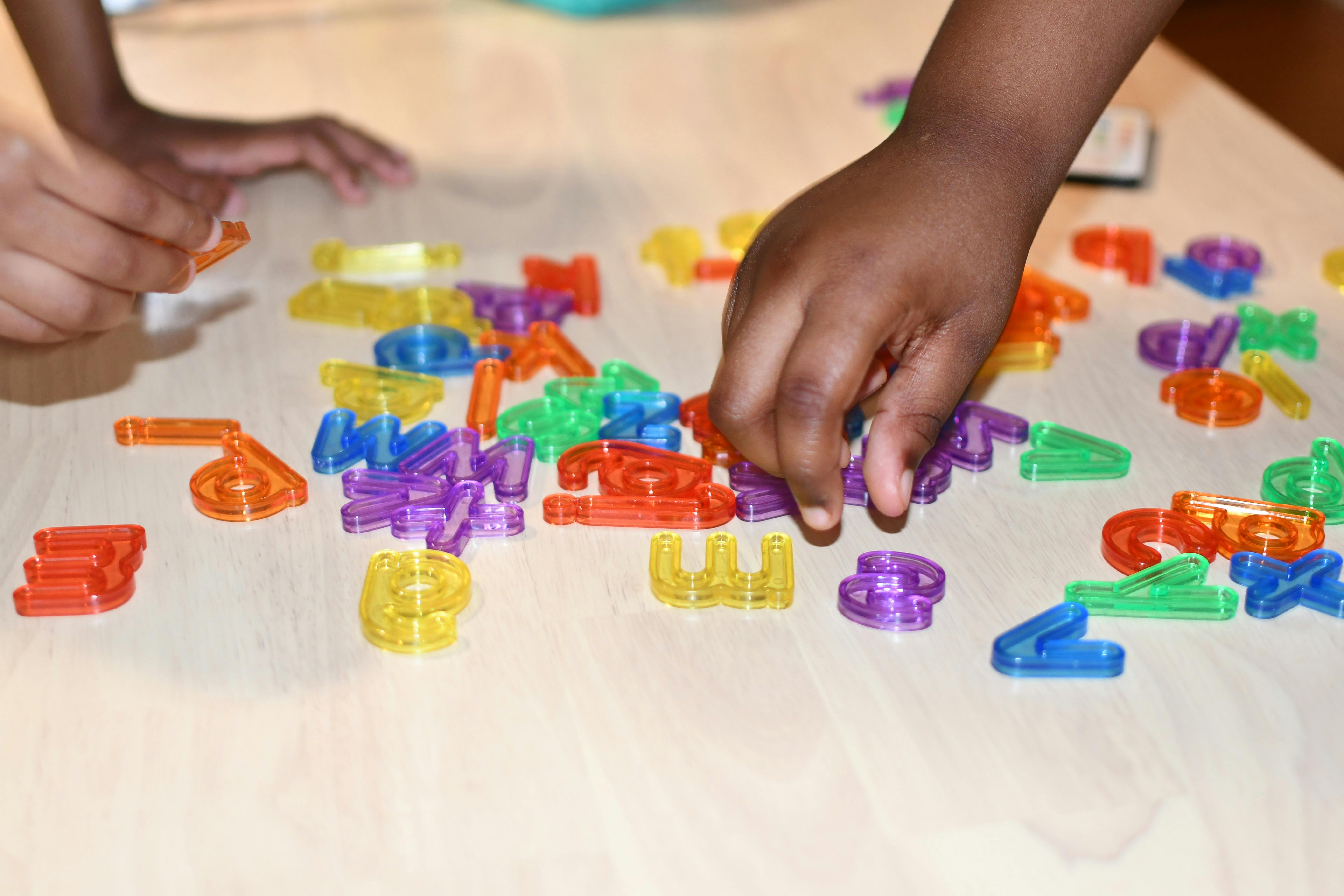 Two children playing with colorful letter-shaped blocks on a table