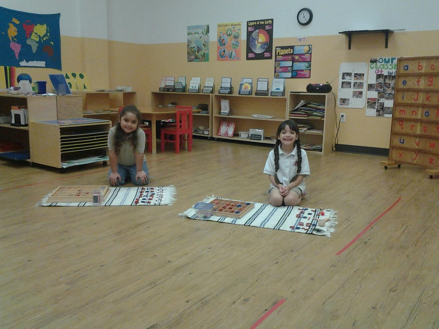 Two children kneeling on mats in a classroom