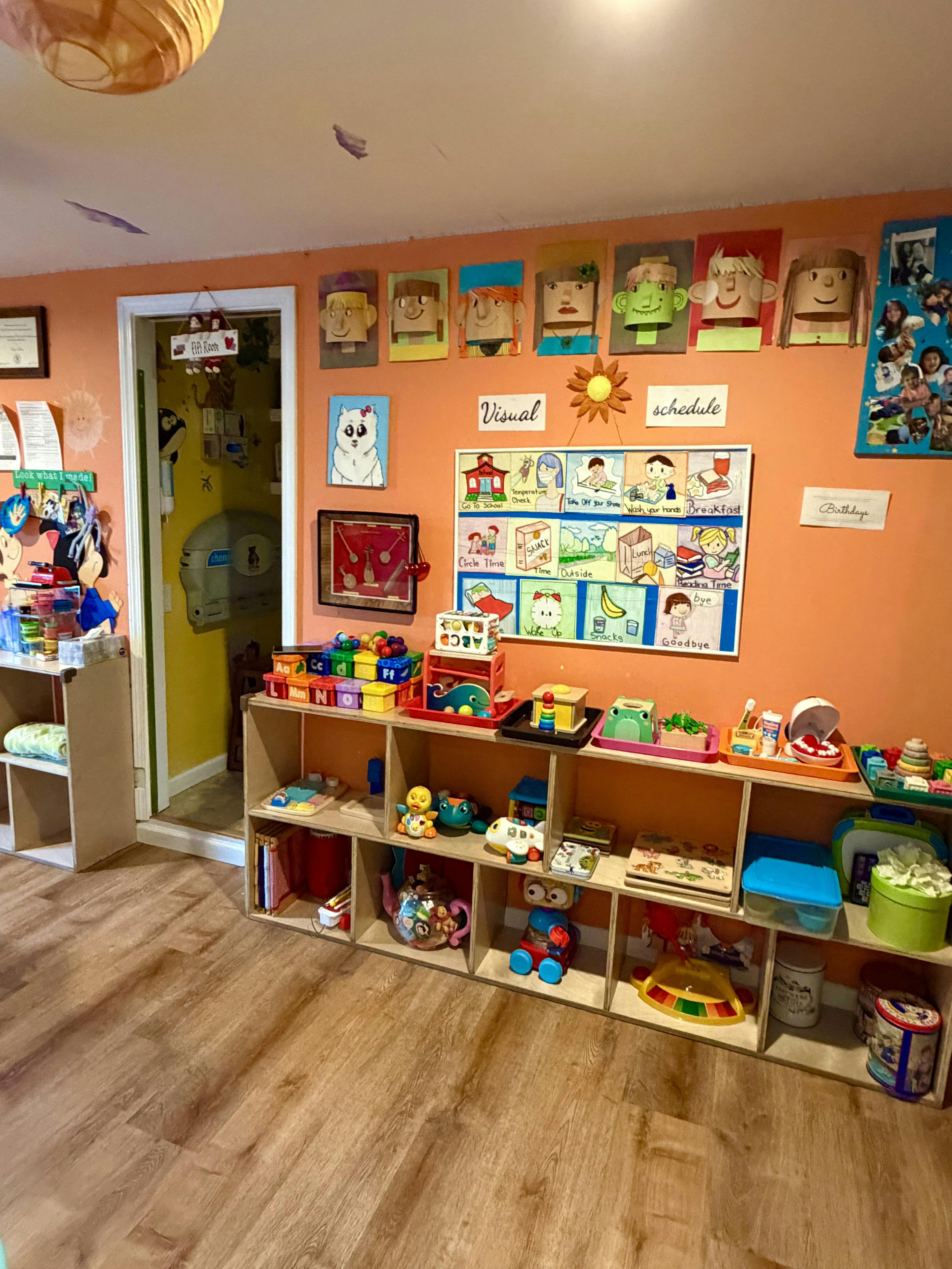 Classroom wall with children's artwork, a visual schedule, and shelves of toys