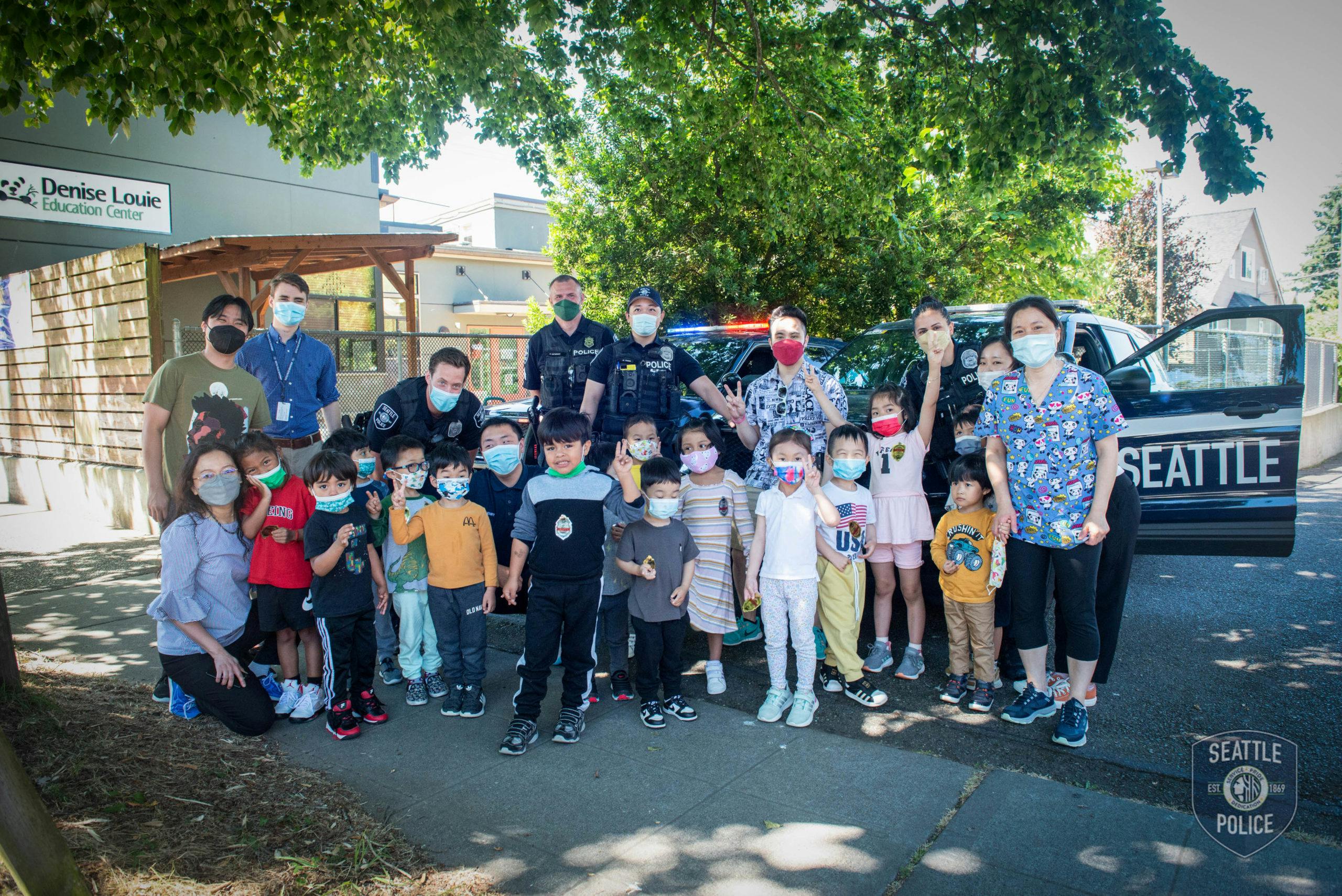 Group of adults and children posing in front of a police vehicle