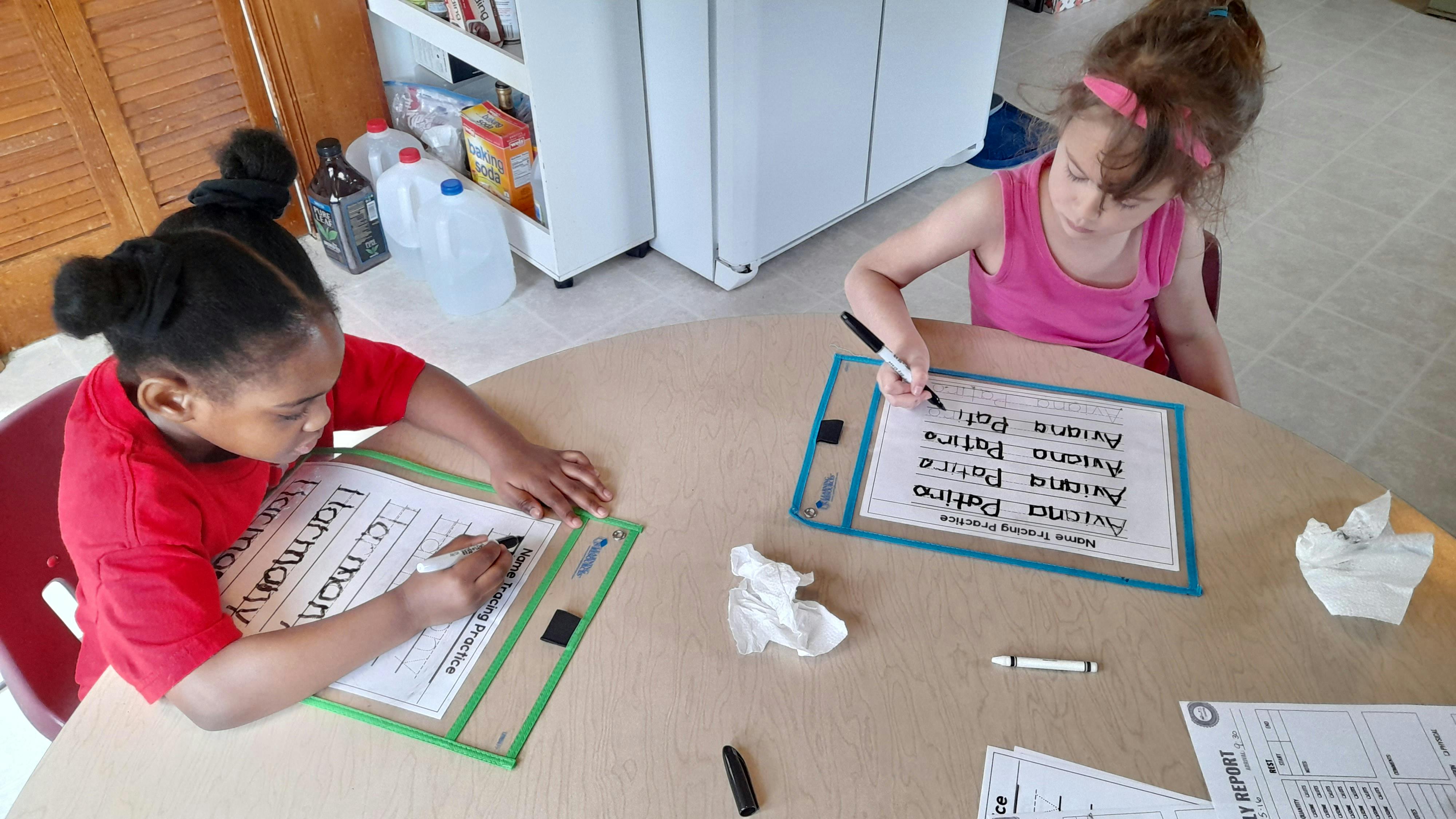 Two children writing on whiteboards at a table