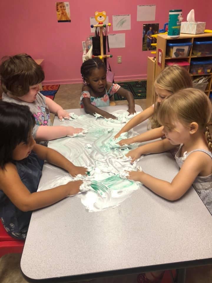 Children playing with shaving cream and green paint on a table