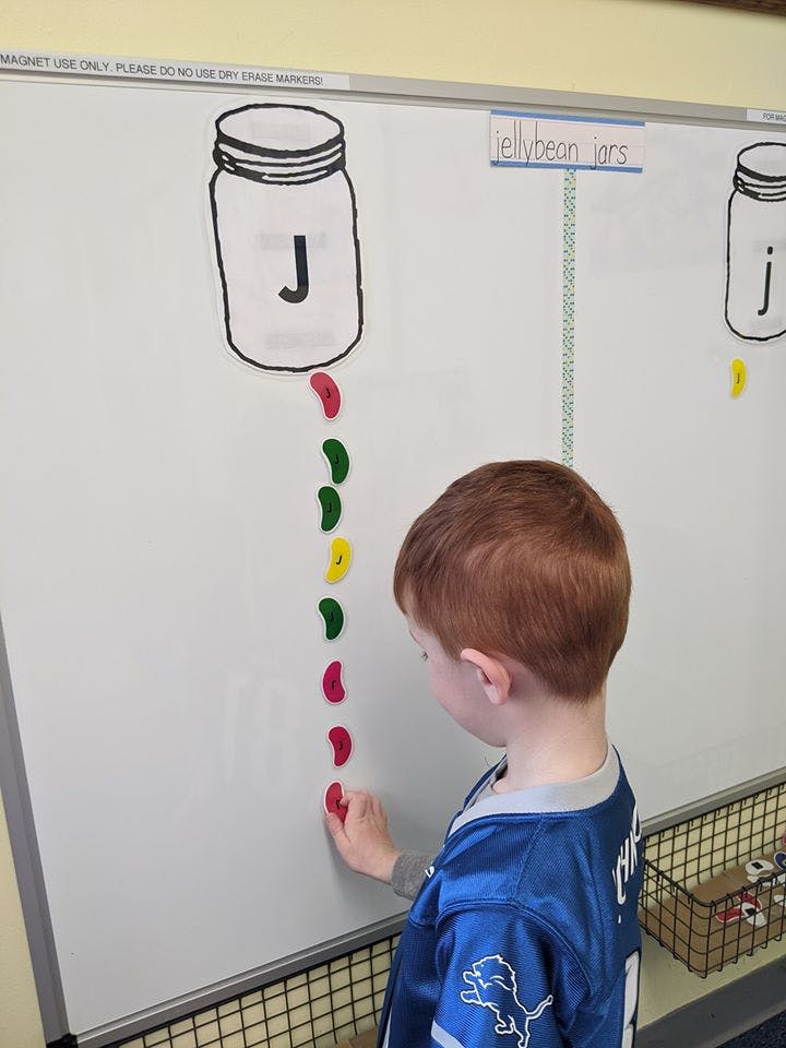 Child placing a red jelly bean shape on a whiteboard below a drawn jar