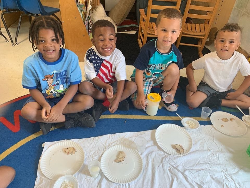 Four children sitting on the floor around paper plates