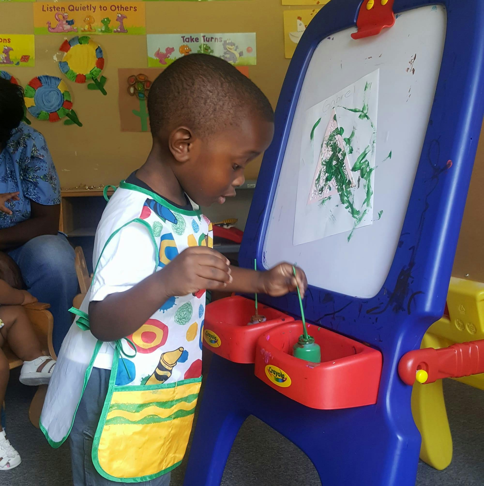 Child in an apron painting at an easel