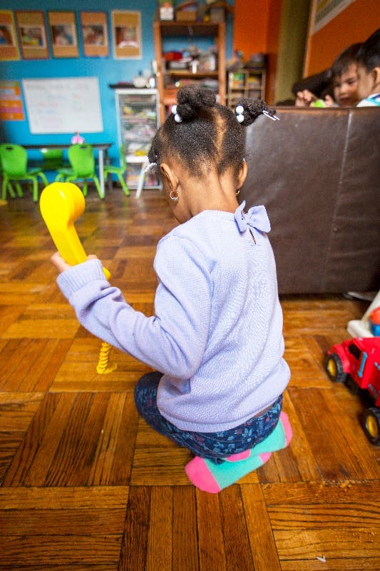 Child sitting on floor holding a yellow toy telephone
