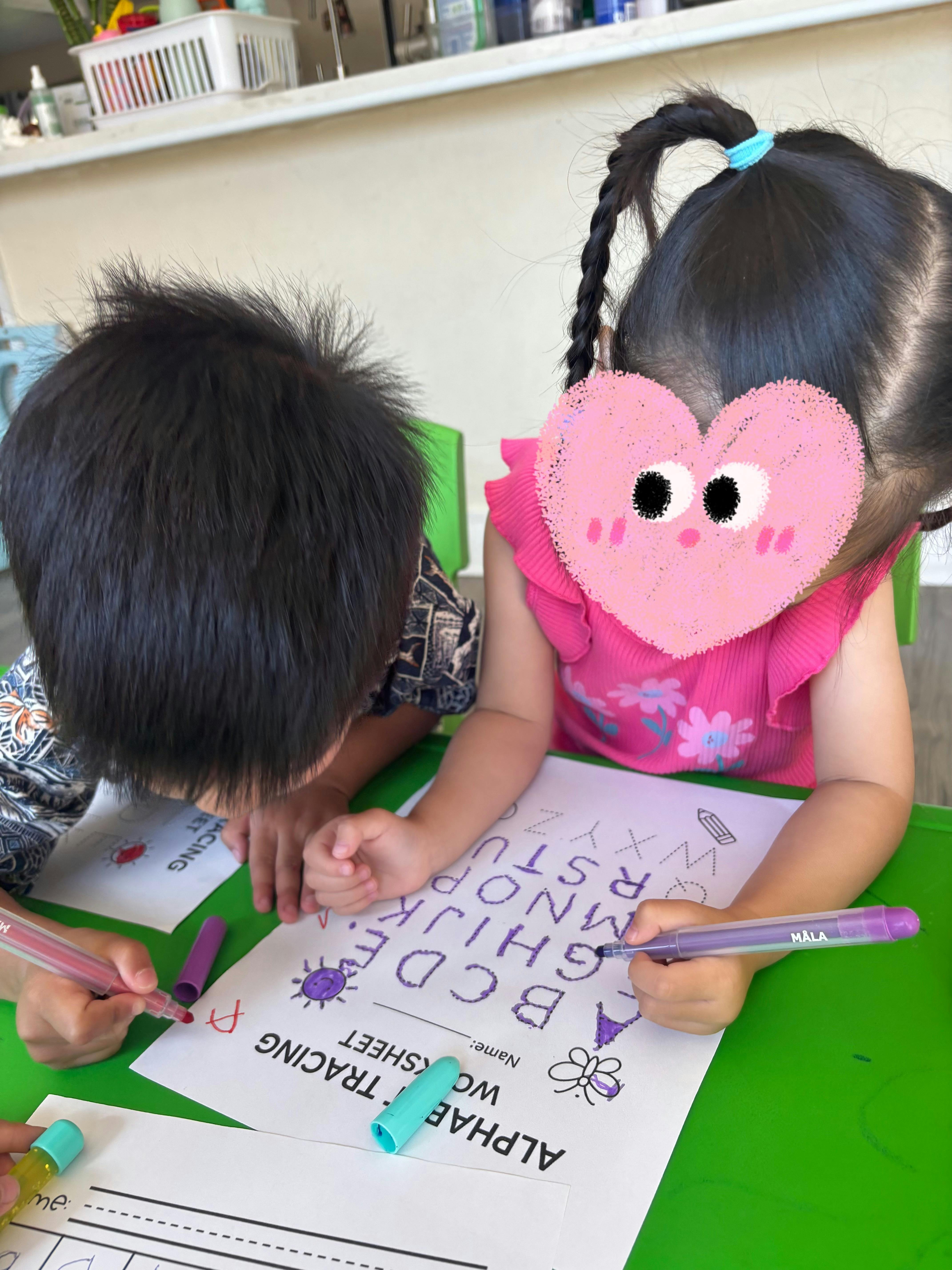 Two children tracing alphabet letters on a worksheet with markers