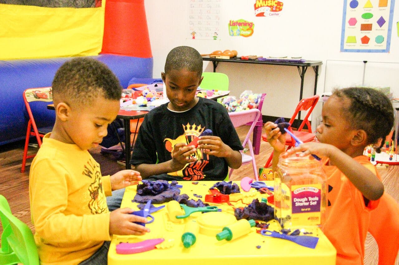 Three children playing with modeling clay at a yellow table