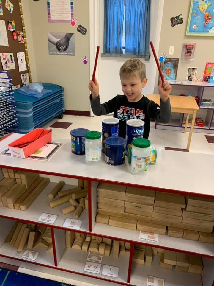 Child playing drums made from containers in a classroom