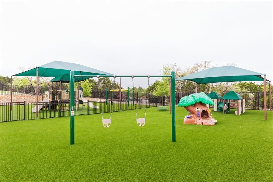 Playground with swings, shade structures, and play equipment on artificial turf