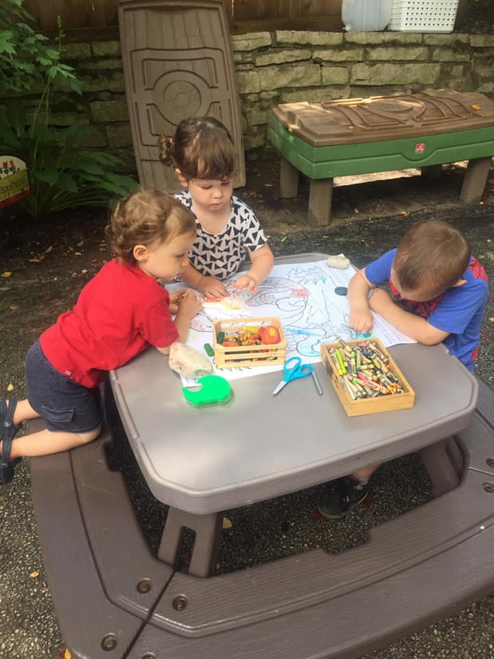 Three children coloring at a small outdoor table