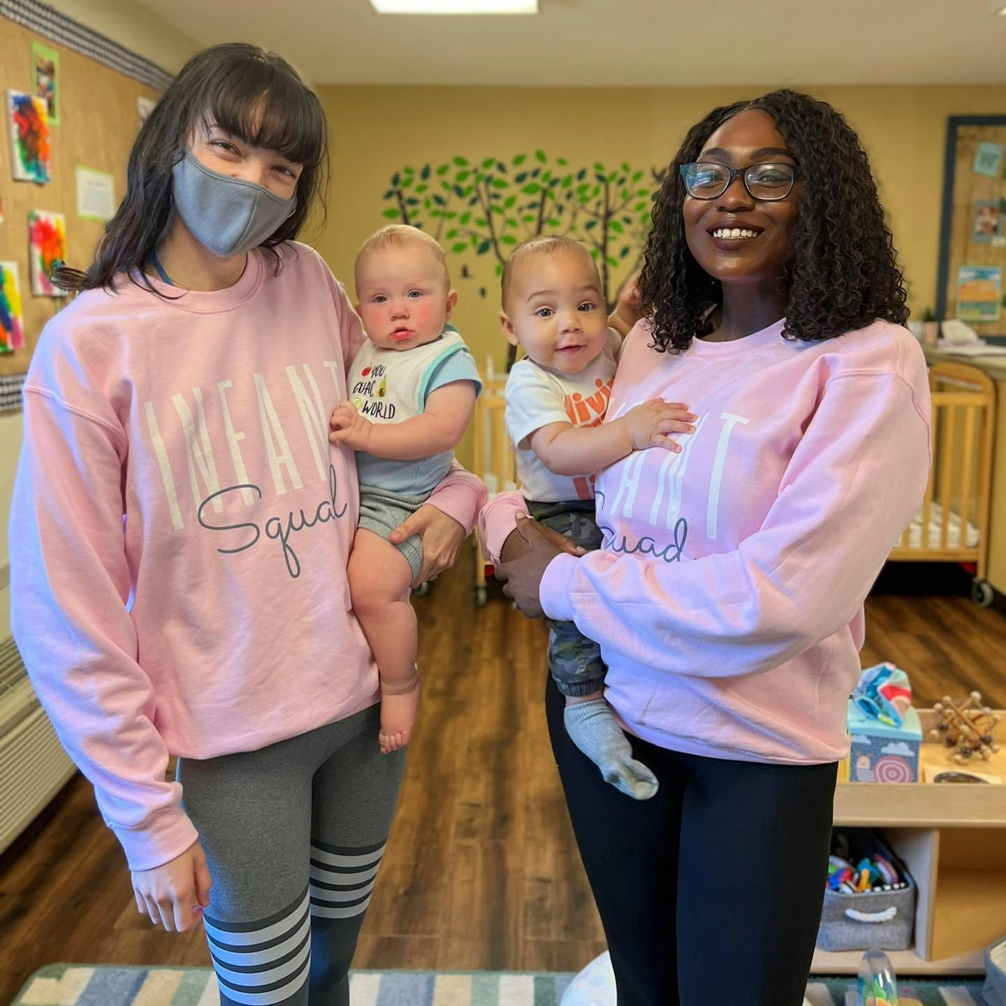 Two people holding two babies in a classroom