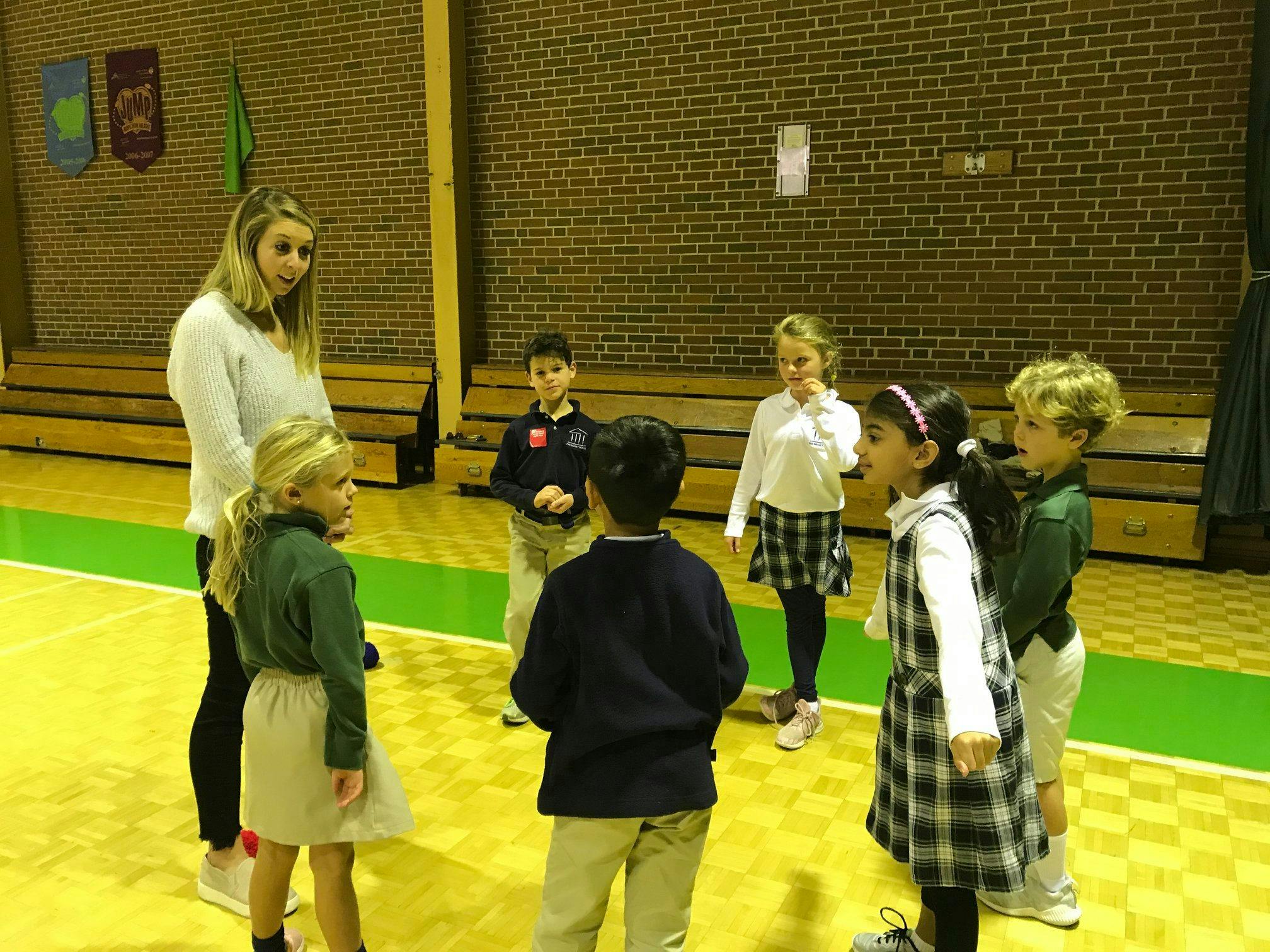 Adult person talking to a group of children in a gym