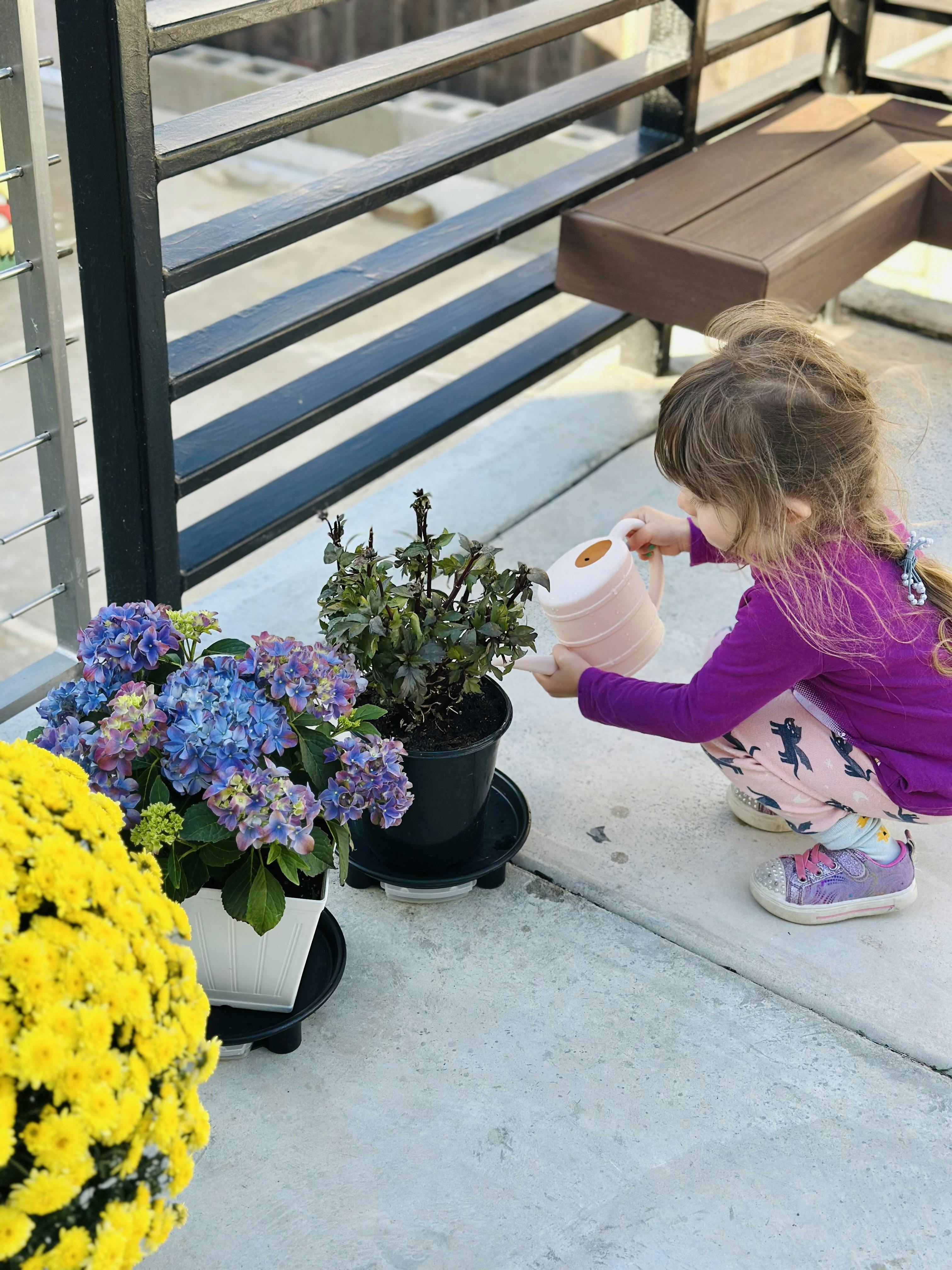 Child crouching to water potted plants with a small watering can