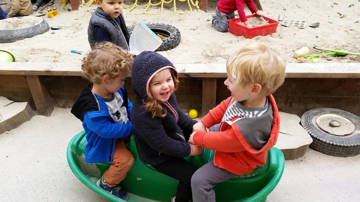 Three children playing on a green seesaw in a sandbox