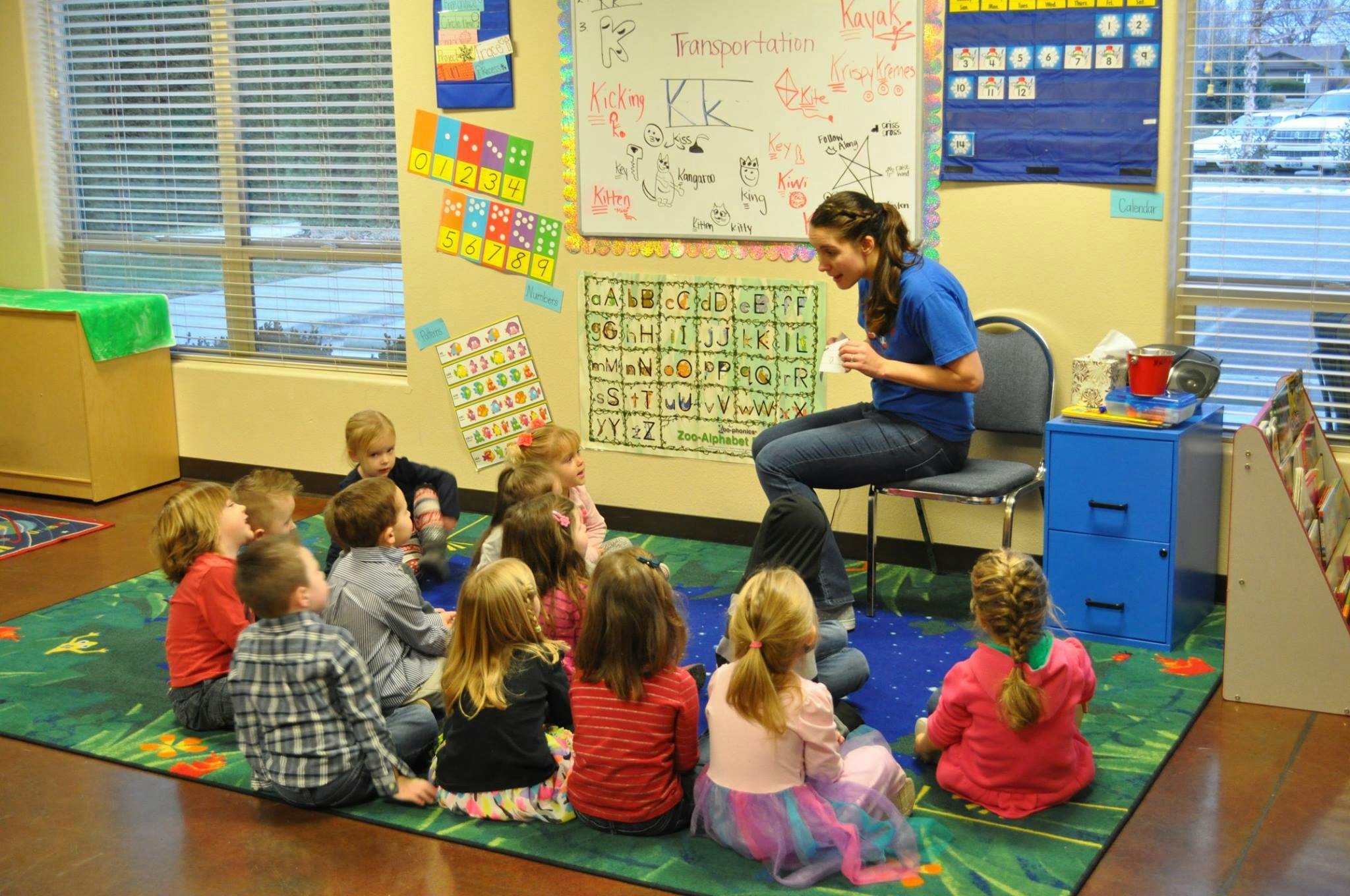 Adult sitting on a chair reading to children sitting on a rug in a classroom