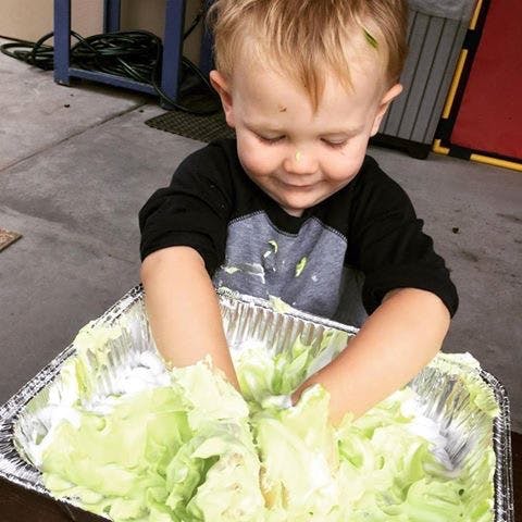 Child playing with lettuce and white cream in a foil pan