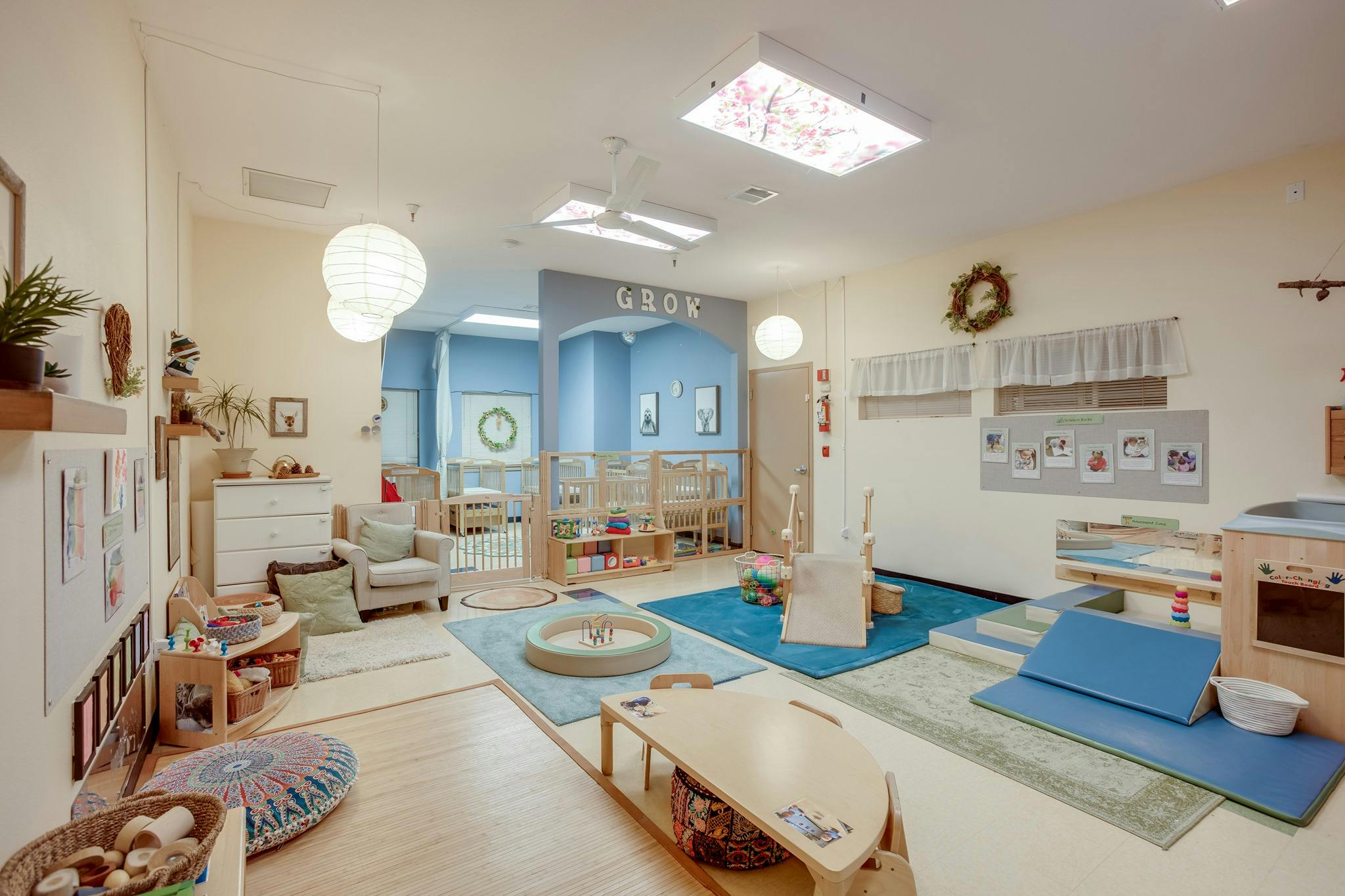 A brightly lit classroom with play mats, small tables, and shelves of a play kitchen