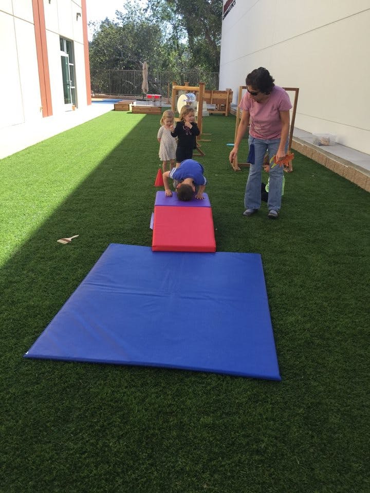 Child on a red and purple mat with a person and two children nearby