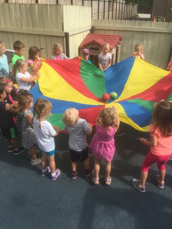 Children playing with a colorful parachute and balls