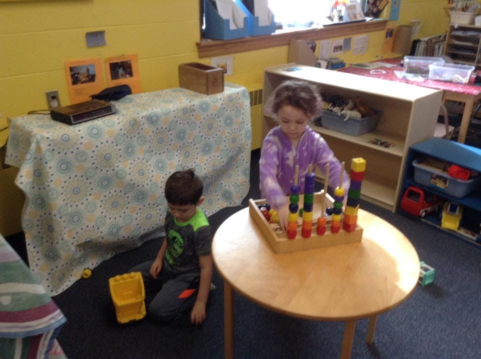 Child playing with blocks at a table, another child on the floor