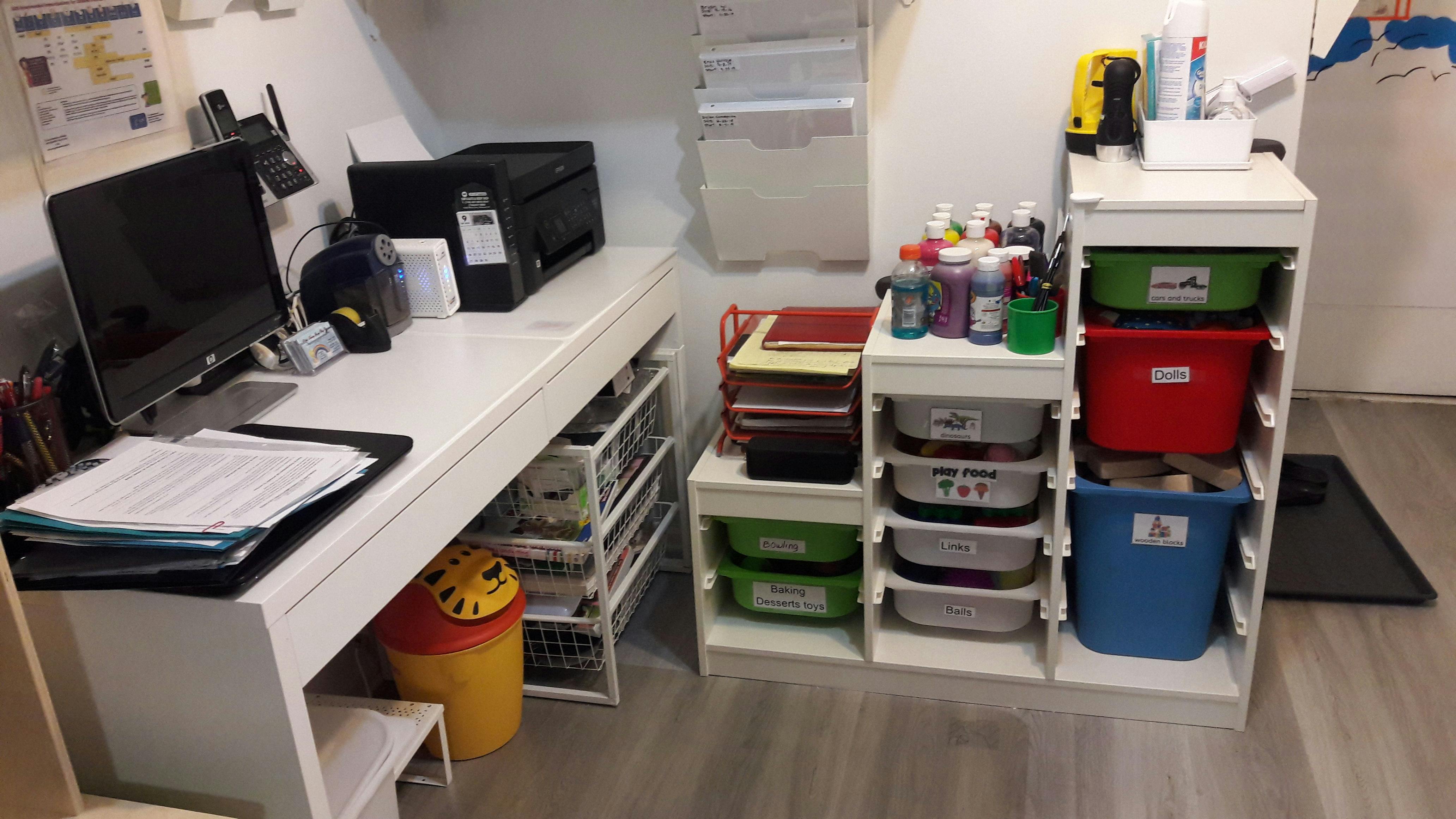 Desk with computer and printer next to storage shelves with bins