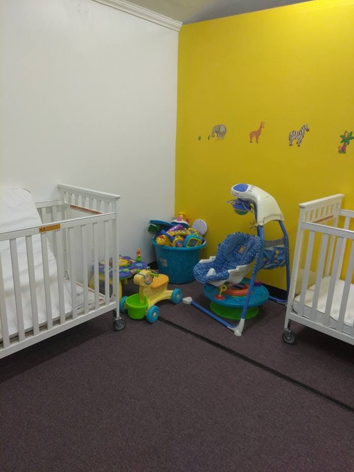 Two cribs, a baby swing, and a bucket of toys in a room with yellow walls