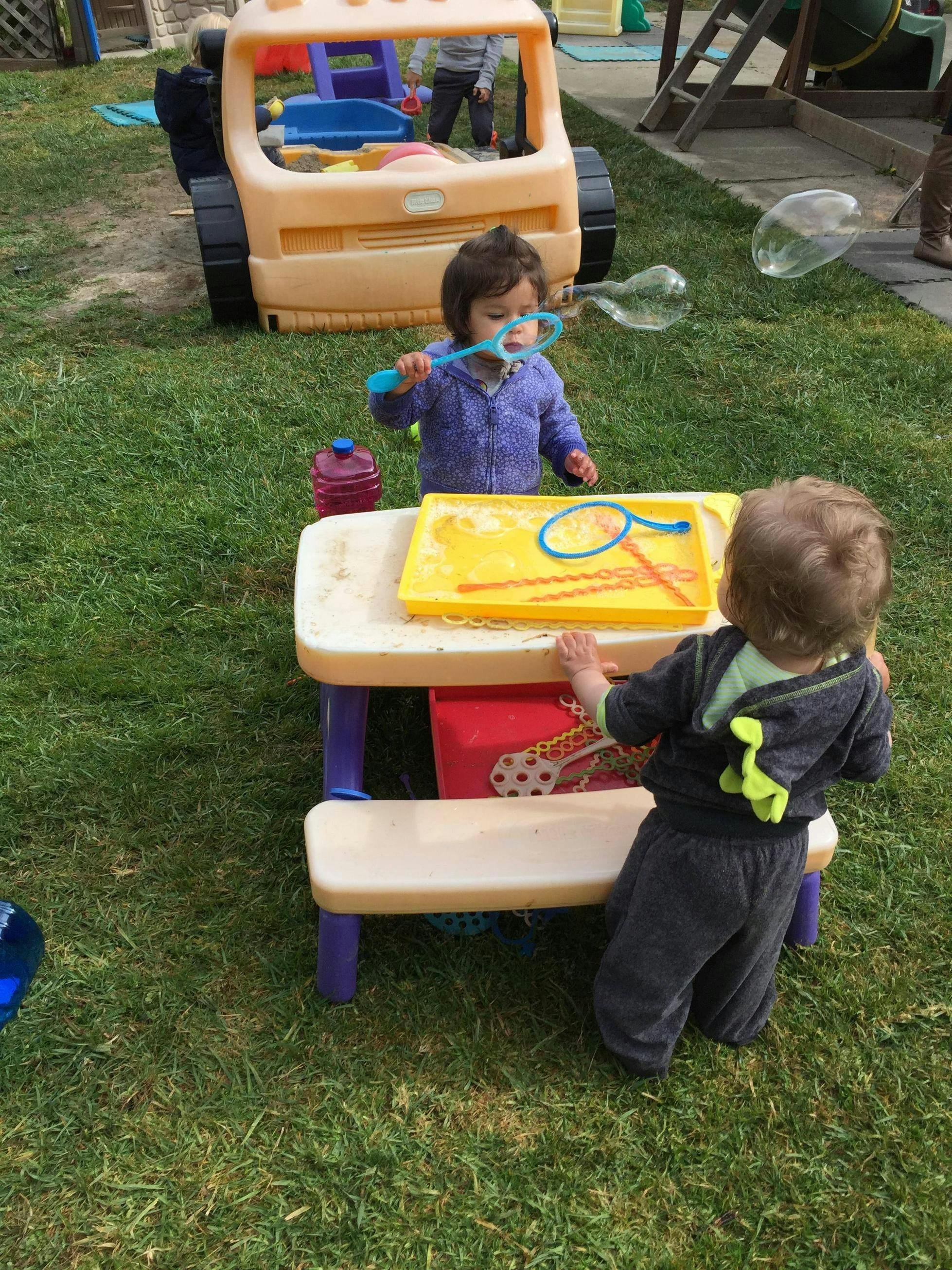 Two children playing with bubbles and a table outdoors