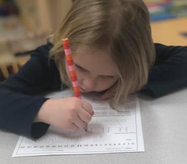 Child writing on a paper with a pencil