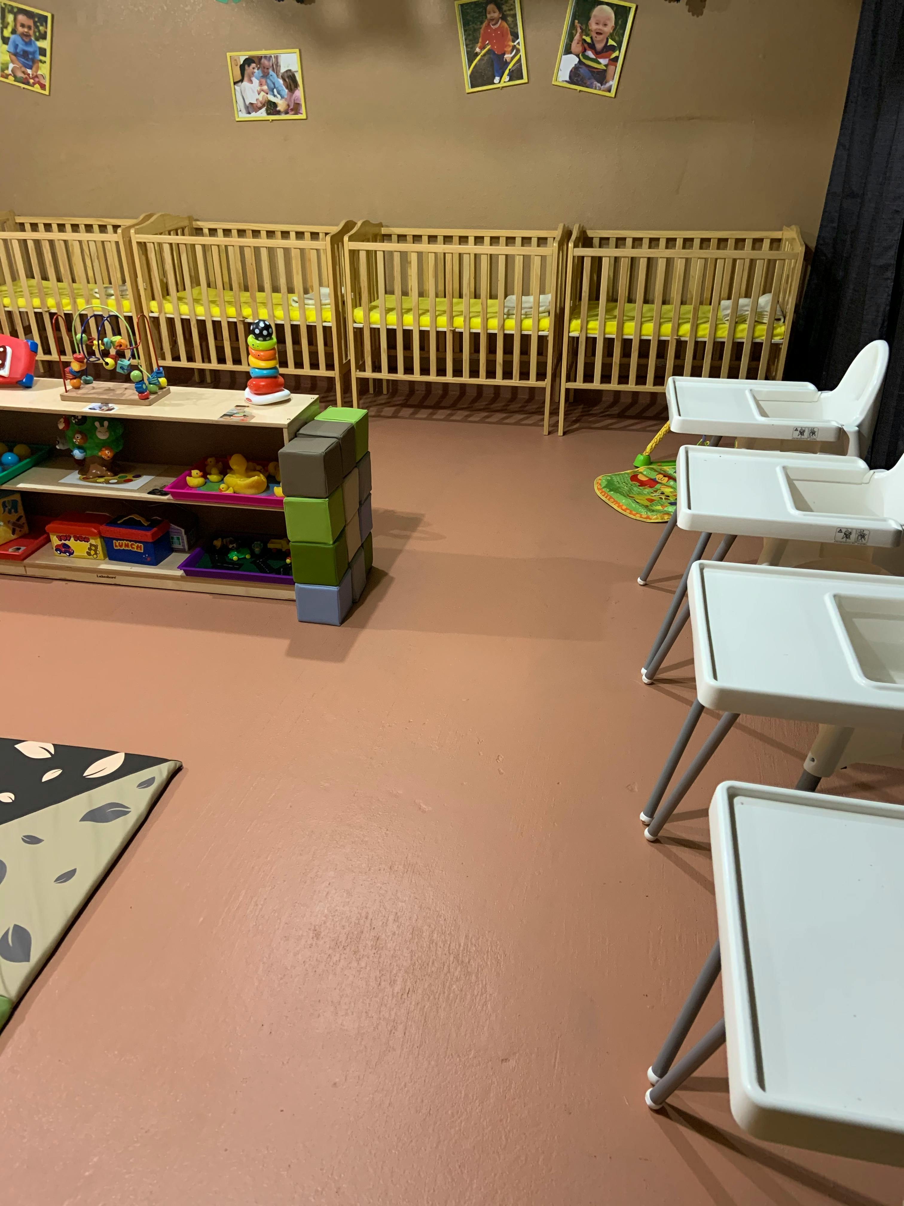 Nursery room with multiple cribs, high chairs, and a toy shelf