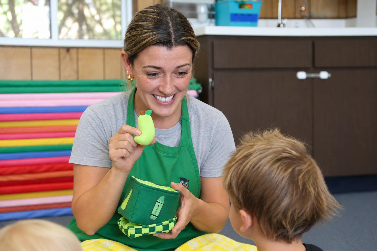 Adult showing a pear-shaped toy to a child in a classroom