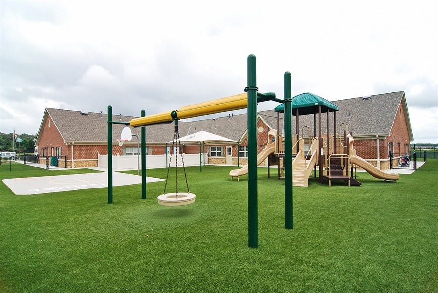 Playground with swings and slides on green grass in front of a building