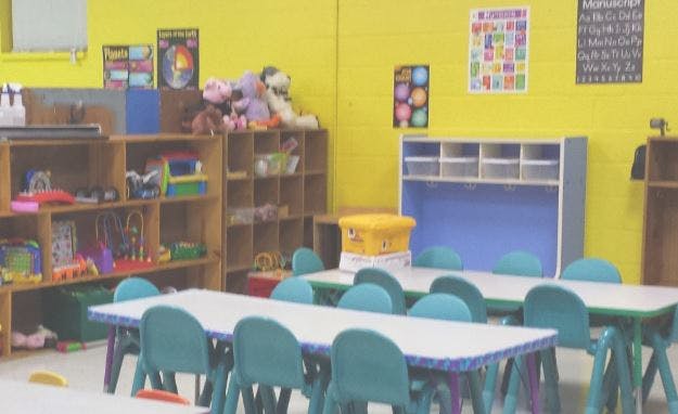 Classroom with small tables and chairs, shelves with toys