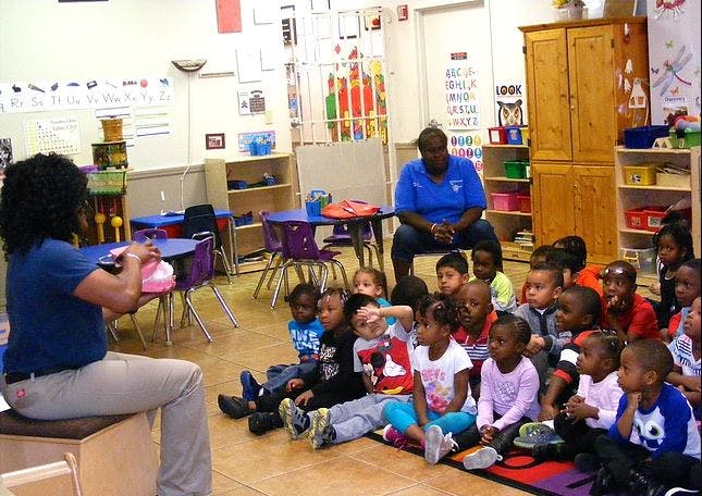 Two people with a group of children sitting on the floor in a classroom