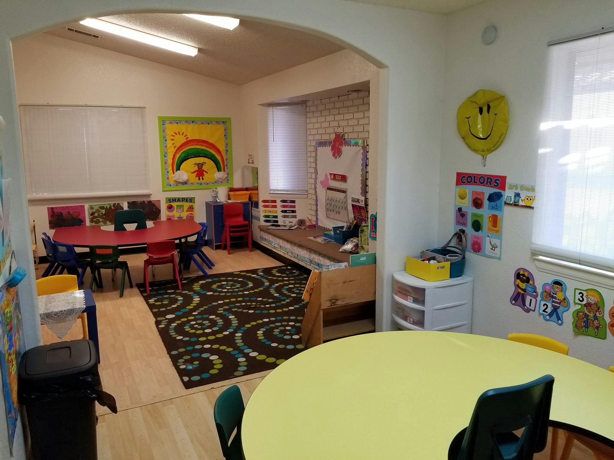 Classroom with small tables and chairs, a patterned rug, and wall decorations
